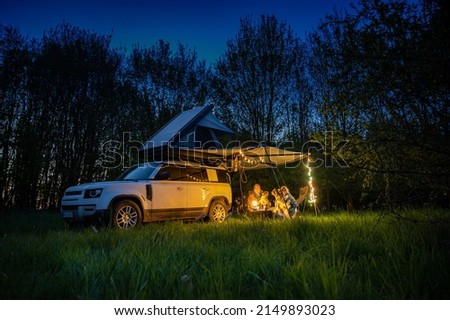 Man and woman with dogs camping in front of a 4x4 Offroad vehicle with roof tent at night time and romantic lighting Royalty-Free Stock Photo #2149893023