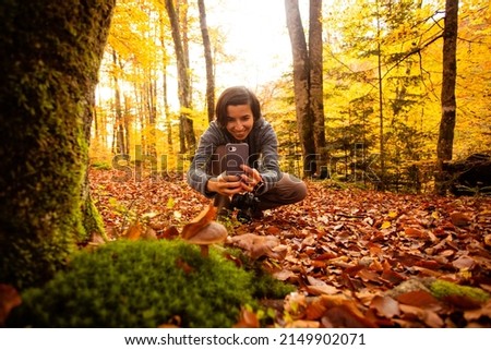 Woman in the forest takes pictures of a mushroom usinag smartphone