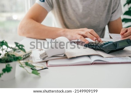 A man counts a bill on a calculator and a check for electricity on the table. Payment of utility services. Saving energy and money concept.  Royalty-Free Stock Photo #2149909199