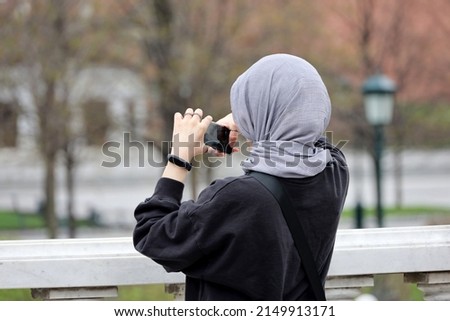 Muslim woman taking photos on smartphone camera on city street. Girl in hijab in spring park