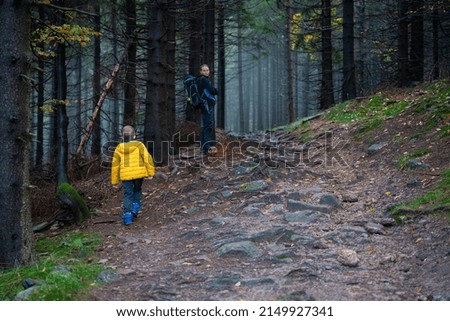 Mum and her little son go on a mountain trail in wet autumn weather.