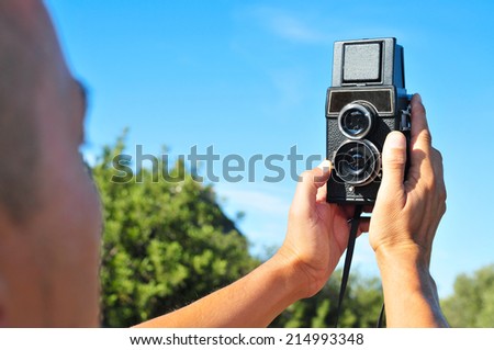 closeup of a young man taking a selfie with an old medium format camera in a natural scenery