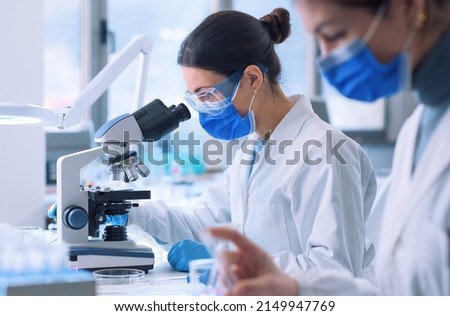 Young researcher looking at the samples under the microscope, she is wearing a face mask and protective equipment Royalty-Free Stock Photo #2149947769