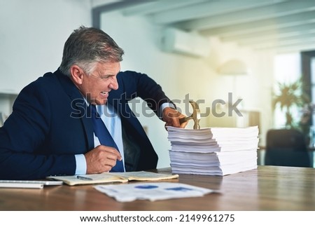 He has an alternative approach to paperwork. Shot of a frustrated businessman hitting a pile of paperwork with a hammer.