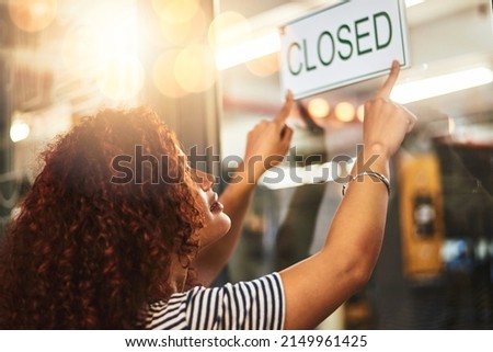 Its the end of another successful day. Shot of a young woman hanging up a closed sign in her store.