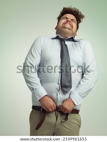 Willing his pants closed. Humorous studio shot of an overweight businessman trying to button his pants. Royalty-Free Stock Photo #2149961655