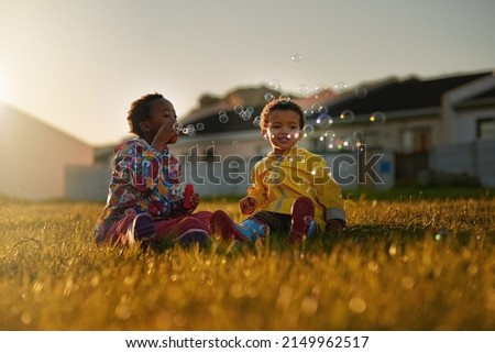 Playing better with bubbles. Shot of a brother and sister sitting on the ground outside blowing bubbles. Royalty-Free Stock Photo #2149962517