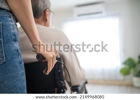 Asian daughter support old disabled man sitting on wheelchair at home. Beautiful girl help and take care of senior elderly mature handicap father patient doing physical therapy in living room in house Royalty-Free Stock Photo #2149968085