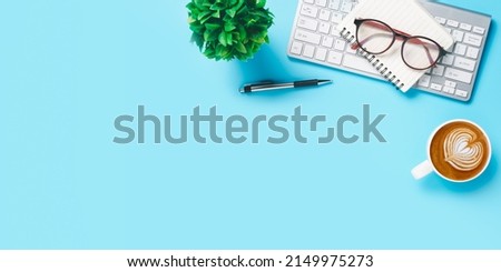 Office desk with keyboard computer, Pen, eyeglass, notebook, Cup of coffee on blue background, Top view with copy space, Mock up.	

