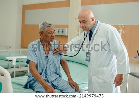 Hospitalized man sitting in bed while doctor checking his pulse. Doctor examining senior male patient in hospital room.