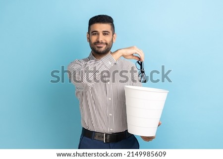 Portrait of smiling happy satisfied businessman throwing out his optical glasses after vision treatment, looking at camera, wearing striped shirt. Indoor studio shot isolated on blue background. Royalty-Free Stock Photo #2149985609