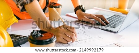 Architect is editing a construction drawing with a pencil.Professional home design Using a laptop in house and building construction projects.Banner cover website design.Expert engineer,worker,coffee.