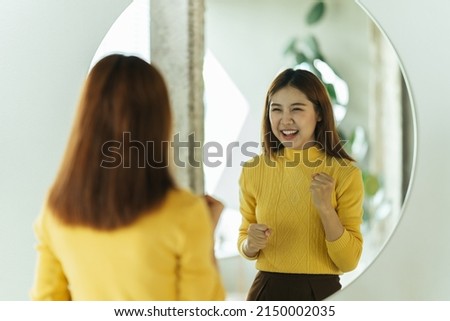 A young Asian woman talks to herself through a mirror to build her self-confidence and empower herself. Royalty-Free Stock Photo #2150002035