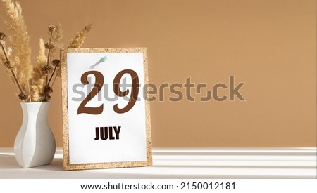 july 29. 29th day of month, calendar date.White vase with dead wood next to cork board with numbers. White-beige background with striped shadow. Concept of day of year, time planner, summer month.