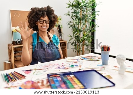 Beautiful african american woman with afro hair painting at art studio showing and pointing up with fingers number five while smiling confident and happy. 