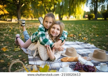 Blonde woman in hat have picnic with daughter in good autumn day. Outdoor portrait of pretty little girl spending time with mother in park.
