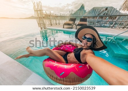 Relaxing woman floating in donut inflatable swimming pool toy at luxury resort taking selfie photo using sunbathing. Travel vacation hotel lifestyle