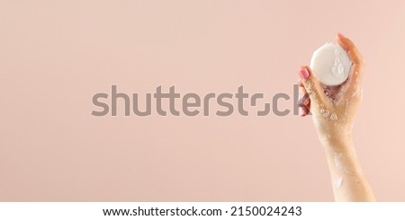 A woman's hand holds a round piece of soap on a light pink background. Banner Royalty-Free Stock Photo #2150024243