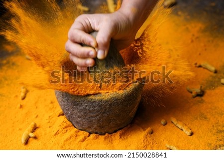 Woman hand powdering Indian spices turmeric powder splash explosion stone mortar Kerala India Sri Lanka traditional Indian kitchen Masala for curry, antiseptic antiviral Ayurvedic medicine. Royalty-Free Stock Photo #2150028841