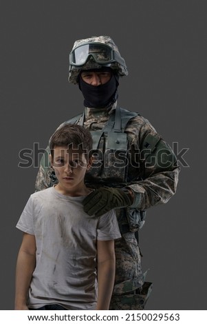 Soldier protecting little kid. Special force army man and young boy against gray background.