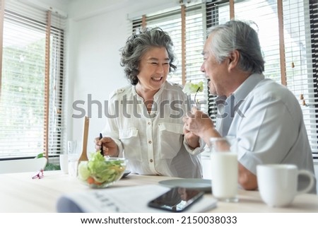 Happy Senior adult couple eating healthy salad together. Lovely Grandmother feeding to her Grandfather. Lover, Retirement, Wellness. BeH3althy Royalty-Free Stock Photo #2150038033