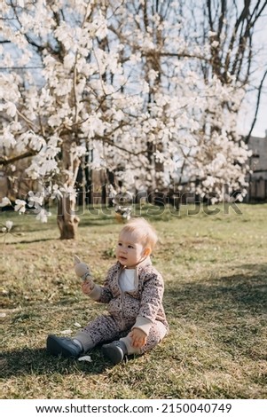 Little baby girl sitting on grass under a magnolia tree in springtime, playing with a bunny.