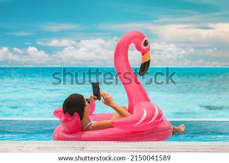 Summer swimming pool vacation relaxing woman floating in flamingo inflatable float using mobile phone at luxury resort sunbathing. Caribbean travel vacation hotel lifestyle Royalty-Free Stock Photo #2150041589