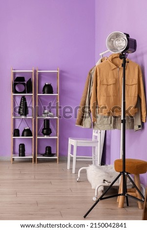 Rack with clothes, shelving unit and lighting equipment in modern photo studio