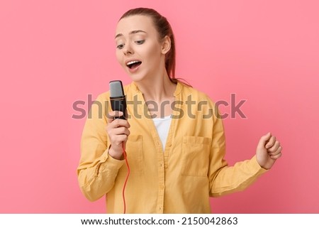 Young woman with professional microphone singing on pink background
