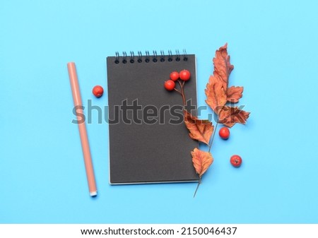 Black notebook, felt-tip pen, dried leaves and berries on color background