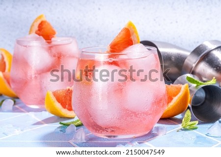Refreshing cold infused citrus water. Detox iced drink with grapefruit slices and mint Pink grapefruit lemonade, summer healthy mocktail or cocktail, on light blue tiled background with bar utensils