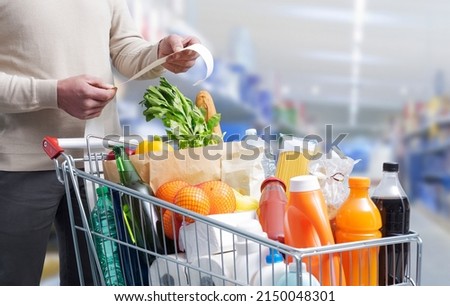 Man standing next to a full shopping cart and checking the grocery receipt Royalty-Free Stock Photo #2150048301