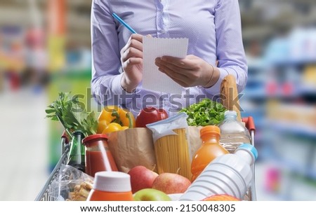 Woman checking a shopping list and buying goods at the supermarket, her shopping cart is full Royalty-Free Stock Photo #2150048305