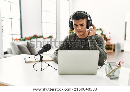 Handsome hispanic man recording podcast thinking attitude and sober expression looking self confident 