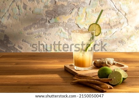 Photo of ginger, galingale lemon soda on a wooden tray with pieces of herb and lemon over abstract colorful wall background. Copy space for text banner. Eatable recipe health herb vegan drink concept.