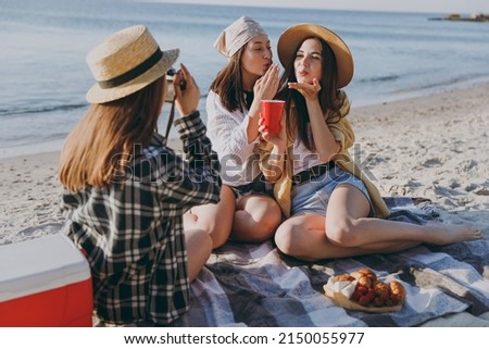 Full size three friends young women in straw hat summer clothes have picnic hang out take photo drink liguor blow air kiss raise toasts outdoors on sea beach background People vacation journey concept