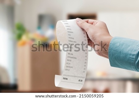 Woman checking a grocery receipt and bag full of groceries in the background Royalty-Free Stock Photo #2150059205