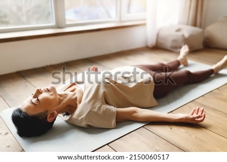 High angle of middle aged barefoot female in activewear lying on floor in Shavasana pose and resting during meditation session in morning at home Royalty-Free Stock Photo #2150060517