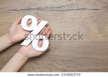 Woman holding paper percent symbol cutout on wooden background, top view. Space for text
