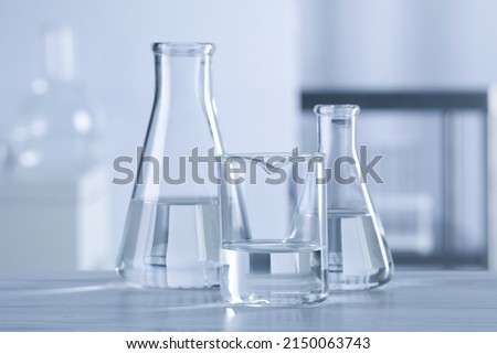 Different laboratory glassware with transparent liquid on wooden table against blurred background