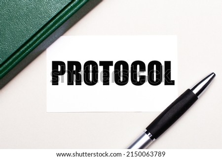 On a light gray background lies a pen, a green notebook and a white card with the text PROTOCOL. Business concept.