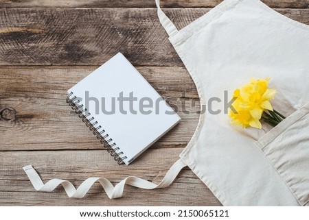Cook book with a bouquet of fresh daffodils on an apron on a wooden background. top view. flat lay