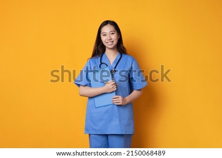 Studio shot of an asian doctor in uniform holding a folder while smiling in a orange background Royalty-Free Stock Photo #2150068489