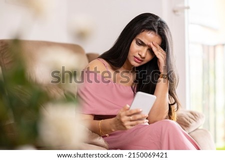 Sad young woman using phone at home.