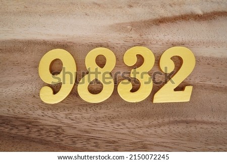 Wooden  numerals 9832 painted in gold on a dark brown and white patterned plank background.