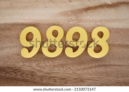 Wooden  numerals 9898 painted in gold on a dark brown and white patterned plank background.
