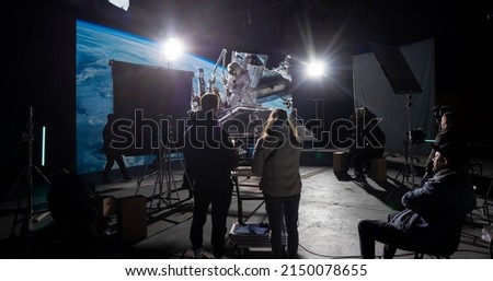 Behind the scenes of virtual production shot - Film crew working with Caucasian female astronaut stuntwoman in a spacesuit hanging on a wires against huge LED screen. Some elements furnished by NASA Royalty-Free Stock Photo #2150078655