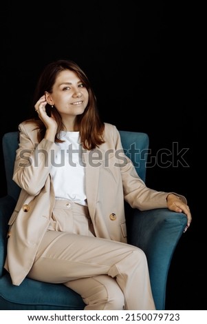 Young beautiful girl posing for a photo. Cute smiling looking at the camera while sitting in a chair in the studio. A business woman is photographed against a black background. High quality photo