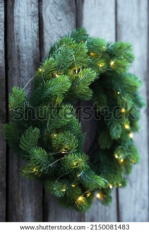 Beautiful Christmas wreath with string lights hanging on wooden wall