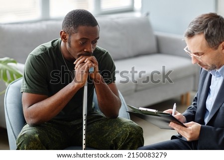 Depressed young adult African American soldier with walking stick treating PTSD with psychotherapy sessions Royalty-Free Stock Photo #2150083279